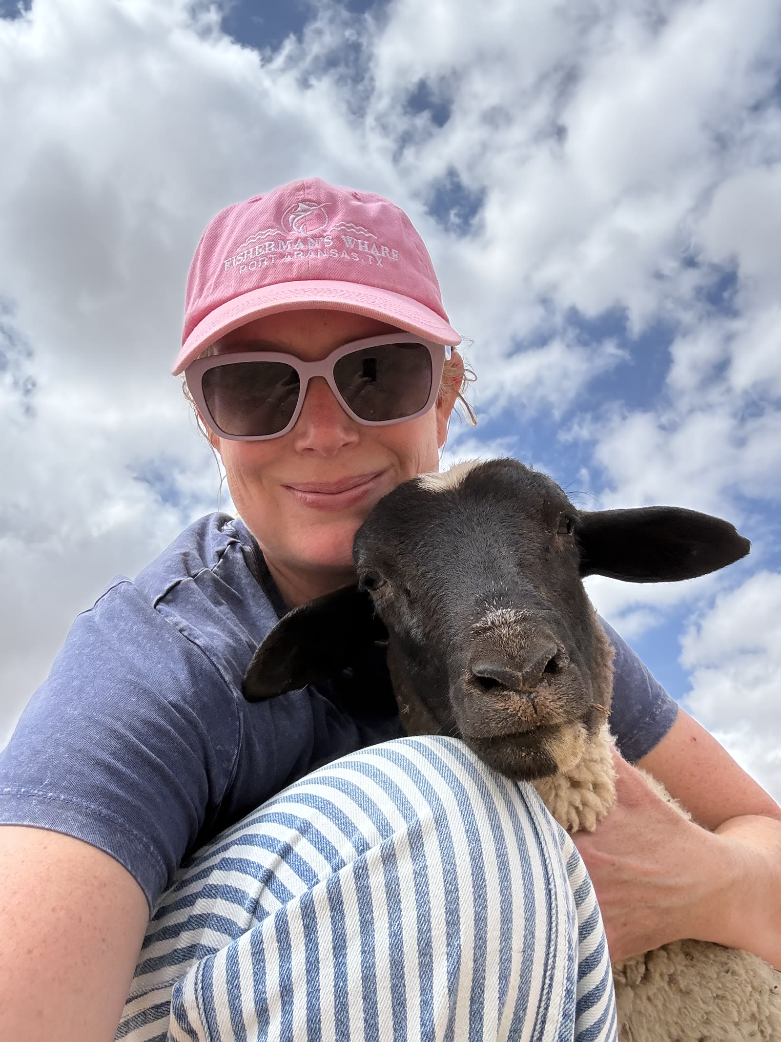 A woman in a pink hat holding a black-faced lamb